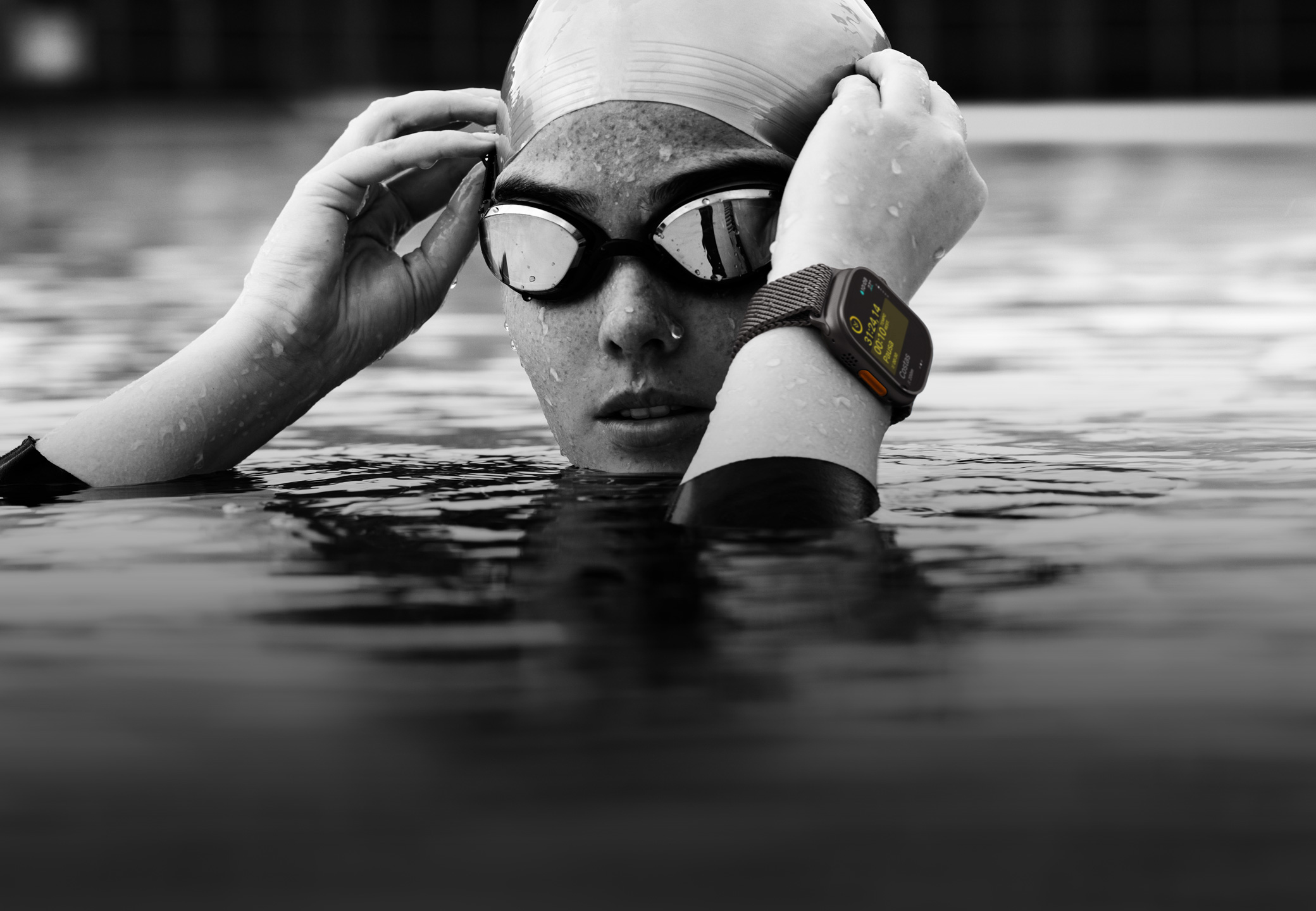 Uma nadadora com o Apple Watch Ultra 2 ajusta os óculos de nata??o em uma piscina. A imagem mostra apenas a cabe?a e as m?os da pessoa.