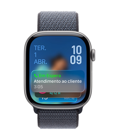 Apple Watch com caixa preta brilhante e pulseira sálvia, com mostrador que exibe uma notifica??o da Assistência de Espera na parte inferior, a data no canto superior esquerdo e os números das horas organizados no canto superior direito.