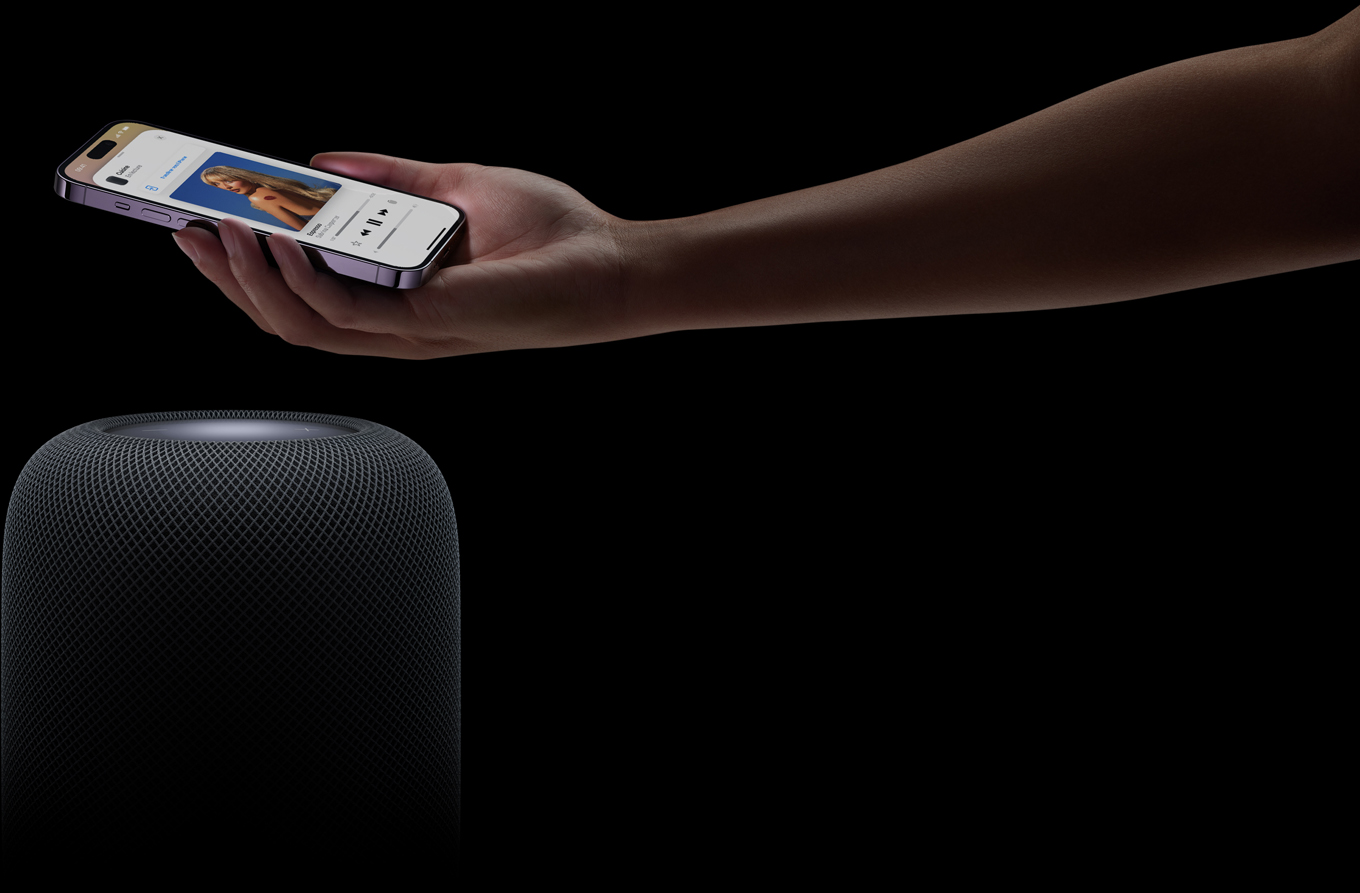 Une main provenant du c?té droit de la page tient un iPhone au-dessus d’un HomePod
