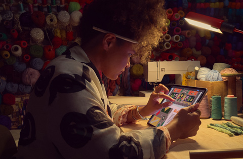 En person, der sidder ved et skrivebord, bruger to fingre p? sk?rmen p? en iPad til at zoome ind p? et billede.