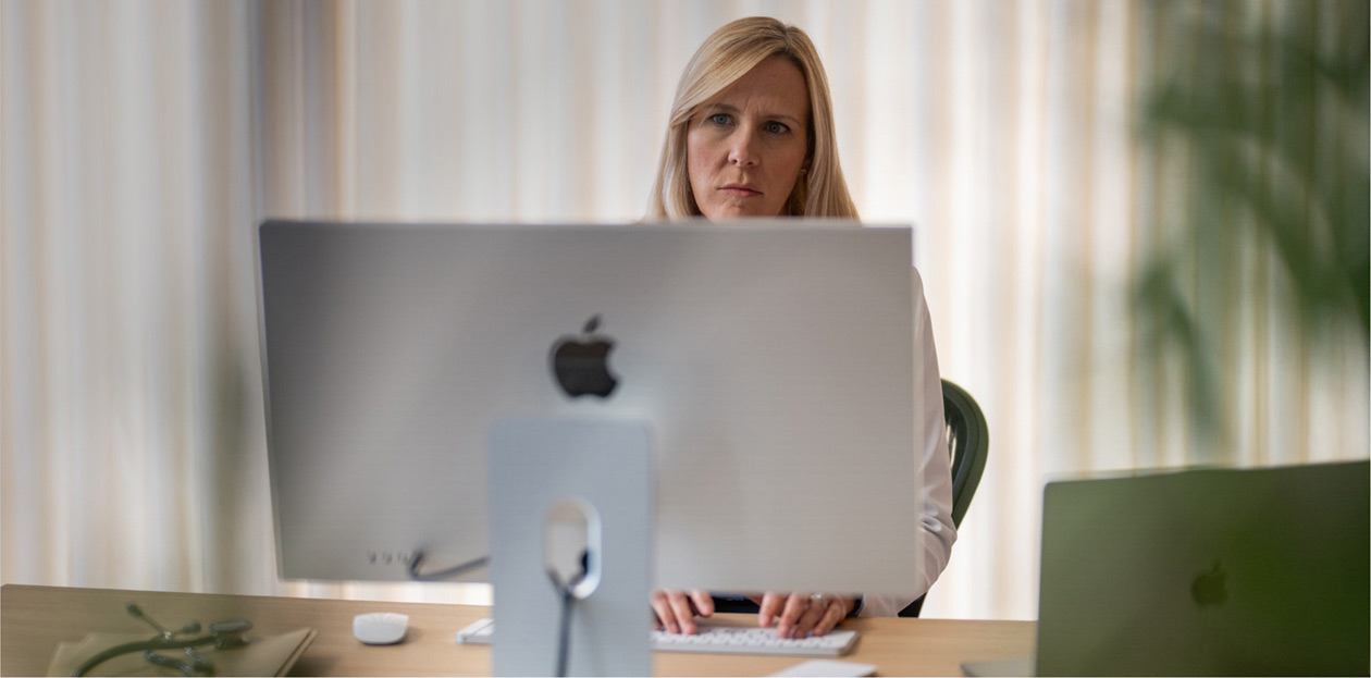 En sundhedsmedarbejder sidder ved sit skrivebord og kigger p? en iMac-sk?rm.