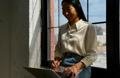 Egy ember az ablaknál ül, mosolyogva nézi a MacBook kijelz?jét.