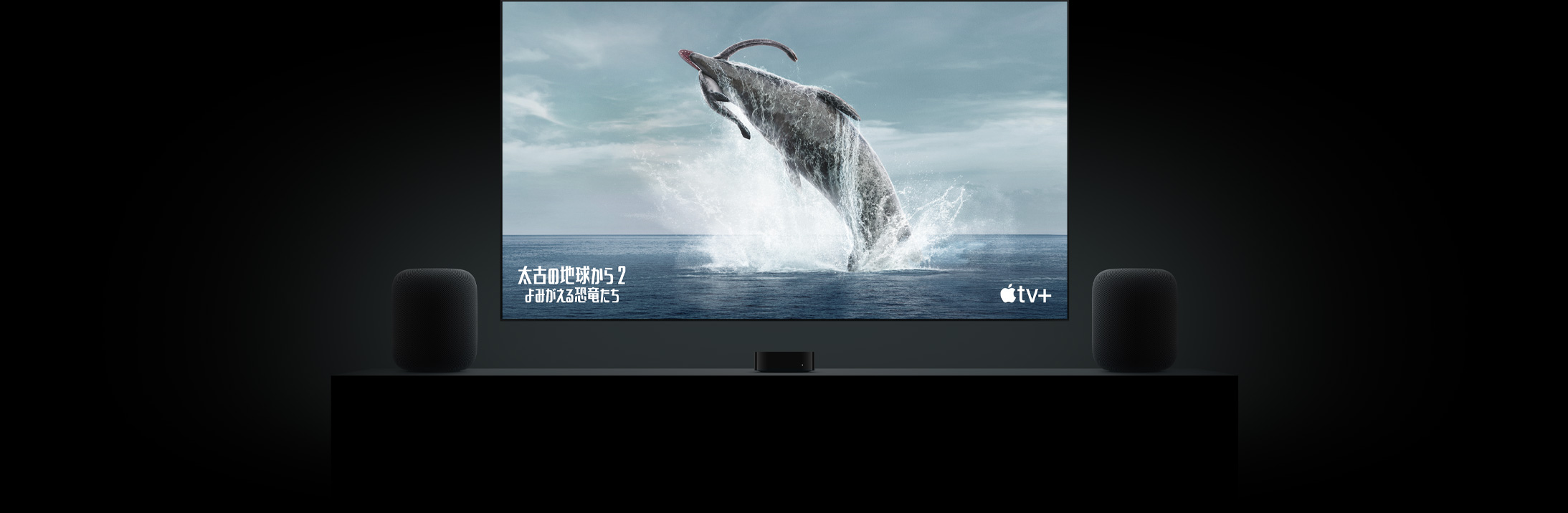 フラットテレビの大きなスクリーン上に「太古の地球から?よみがえる恐竜たち?」の恐竜の鮮明な映像が映し出されている。リビングルームのキャビネットの上に置かれた2臺(tái)のHomePodスピーカー。その間にApple TVが配置され、その上にテレビが掛けられている