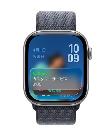 グレイのバンドを組み合わせたスペースグレイのApple Watch。畫面の下部に保留アシスタントの通知、左上に日付、右上に上下に重なった時刻が表示されている