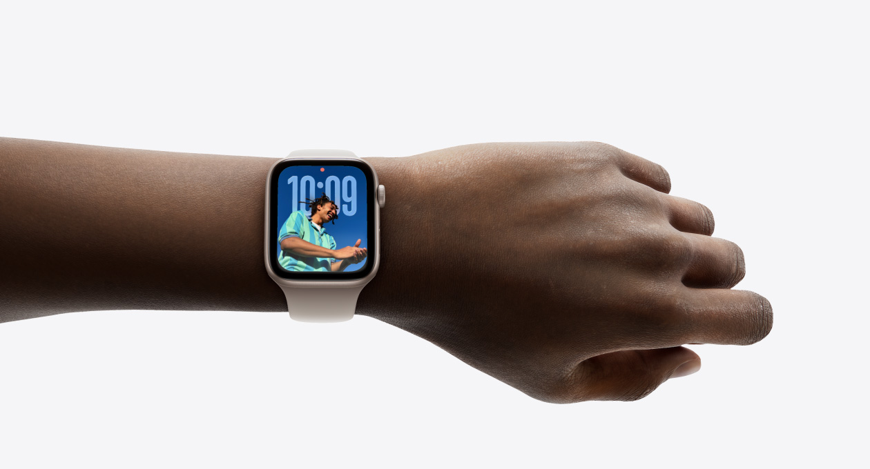 Close-up of Apple Watch in Silver with rubber band on a person’s wrist, showing Time app in new Liquid Glass design
