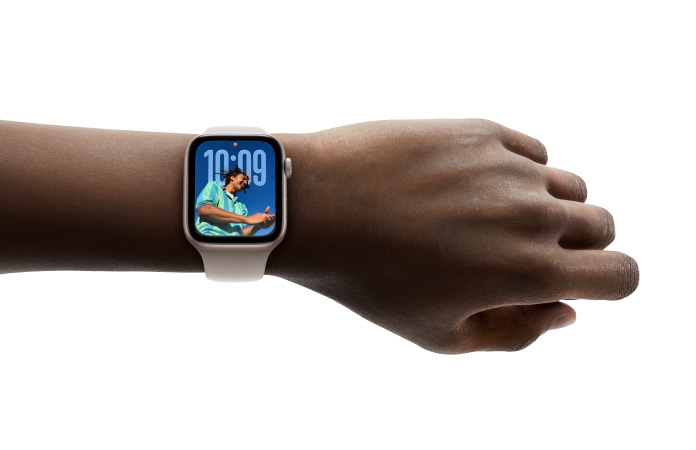Close-up of Apple Watch in Silver with rubber band on a person’s wrist, showing Time app in new Liquid Glass design