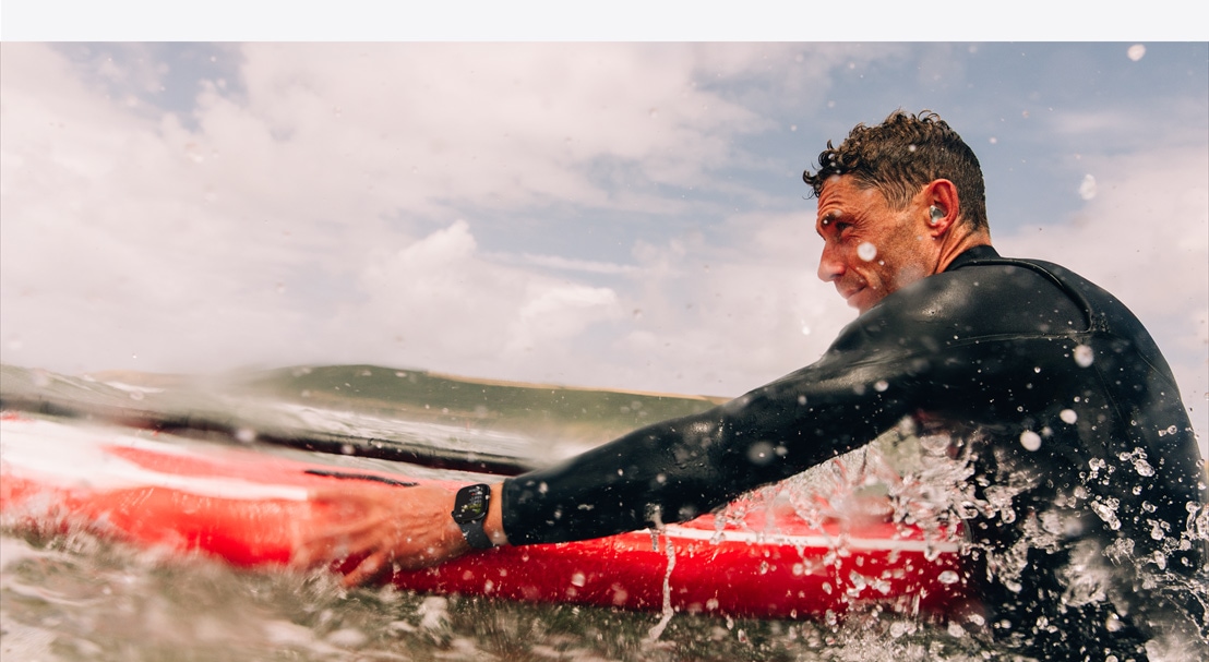 A man in a wetsuit wearing an Apple?Watch?Series?10 preparing to paddle out in the surf.