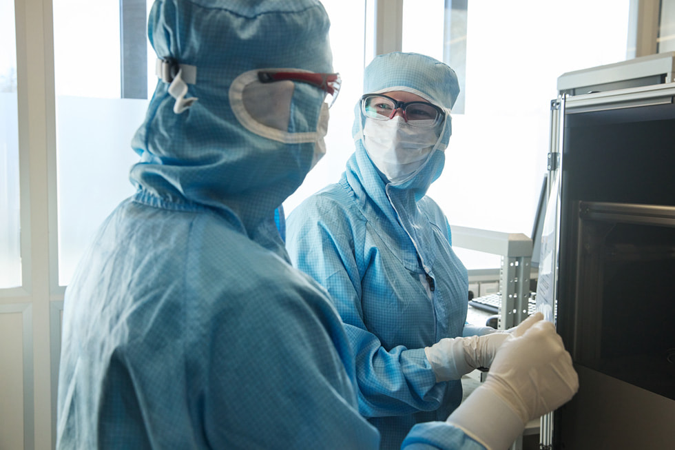 Two technicians at TRUMPF Ditzingen wearing protective clothing look at one another in a lab-like setting.
