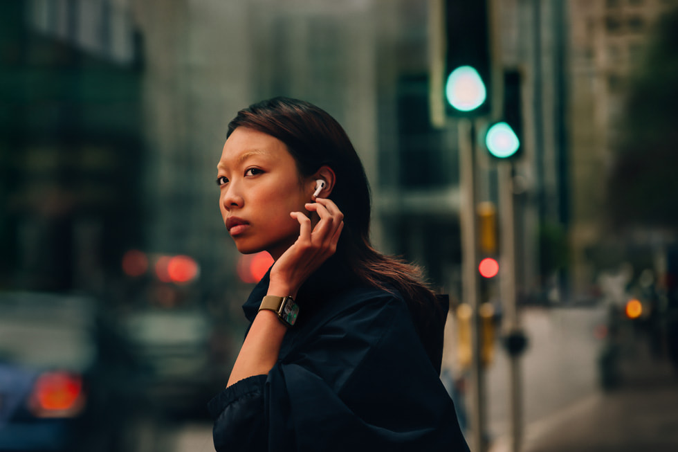 Seseorang mengenakan AirPods 4 dan Apple Watch Series 10 berdiri dipinggir jalan kota.