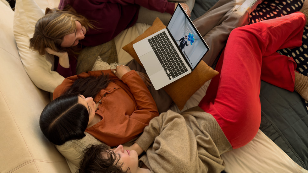 Drie mensen die op een bank zitten en naar ‘Severance’ kijken op een MacBook?Air.