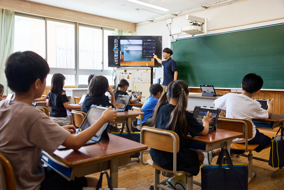 京都市の小學(xué)校の教室で前方で授業(yè)をする教師と、席でiPadを使いながらそれを見ている子どもたち。