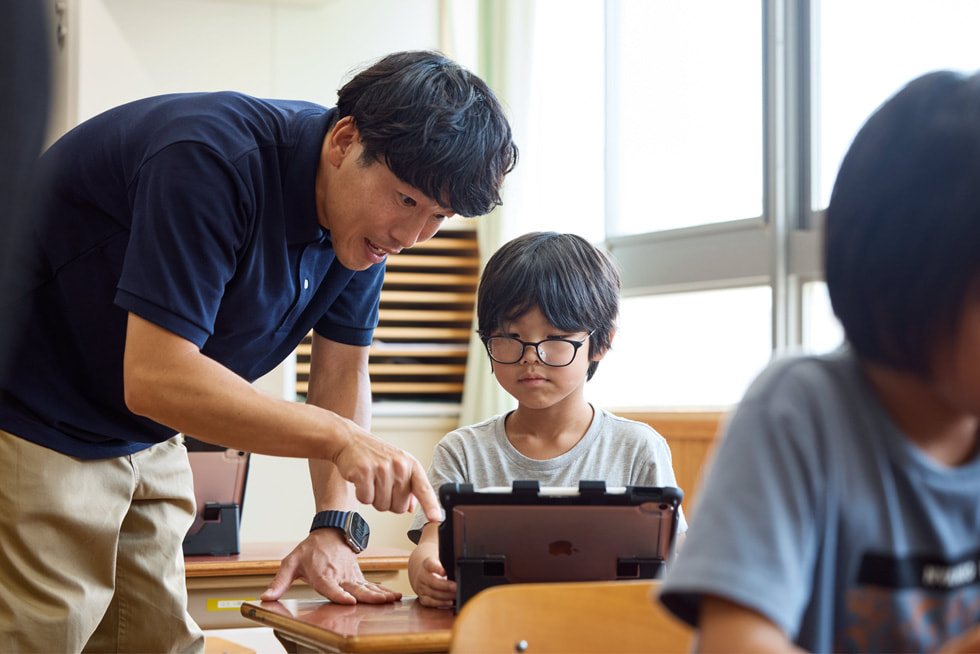 京都市の小學(xué)校の教室で、機(jī)でiPadを使って子どもと一緒に作業(yè)する教師。