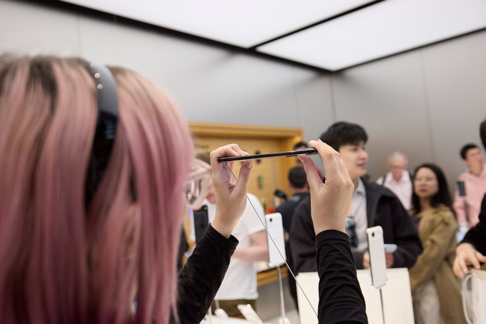澳洲 Apple Sydney 零售店內，一位顧客手持 iPhone Air 仔細查看。