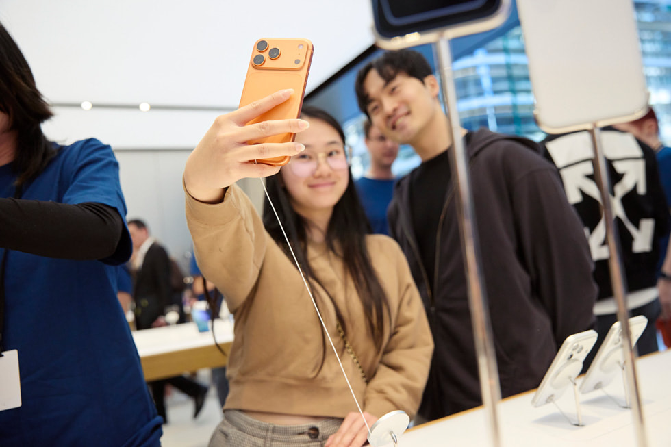 澳洲 Apple Sydney 零售店內，兩位顧客開心地手持 iPhone 17 Pro 自拍。