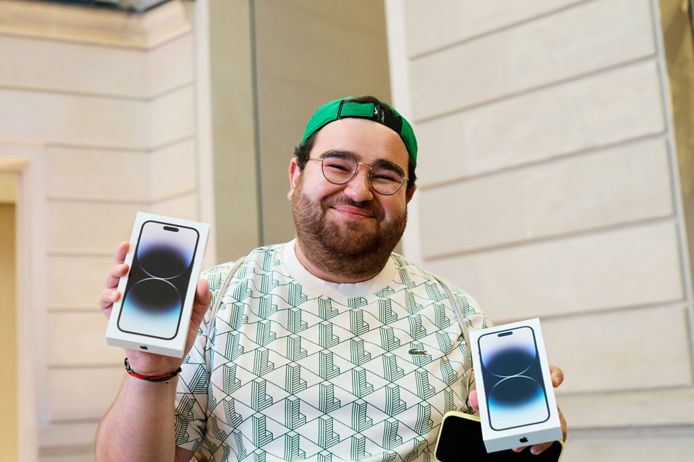 A customer standing outside of Apple Champs-élysées looks at a window display featuring different iPhone devices.