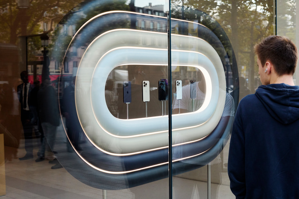 A customer at Apple Champs-élysées holds up two boxed devices from the iPhone 14 lineup.