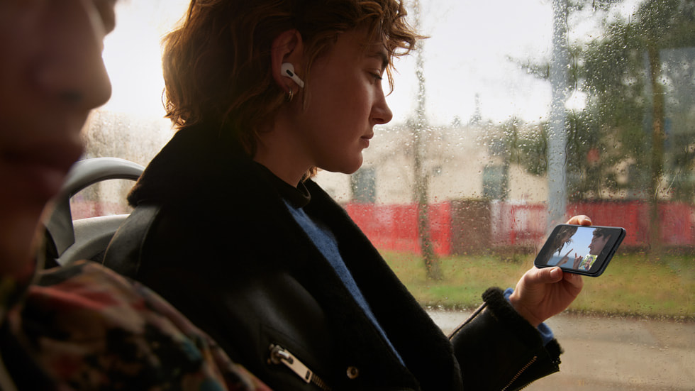 Otobüste kula??nda AirPods’la iPhone’da 5G kullanarak SharePlay ?zelli?iyle video izleyen bir k?z.