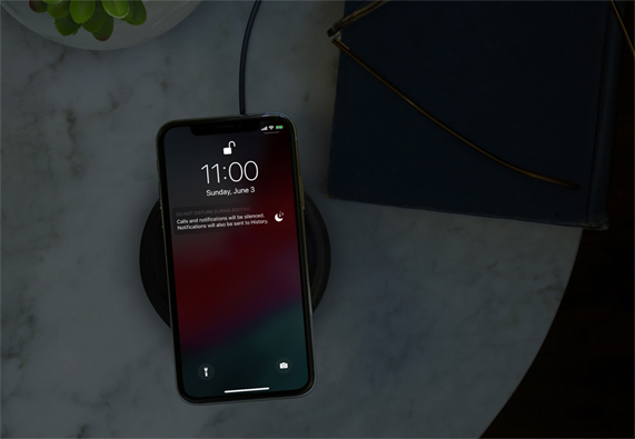 Karanl?k bir odada, kablosuz ?arj cihaz?nda duran iPhone, Rahats?z Etme modunda. 