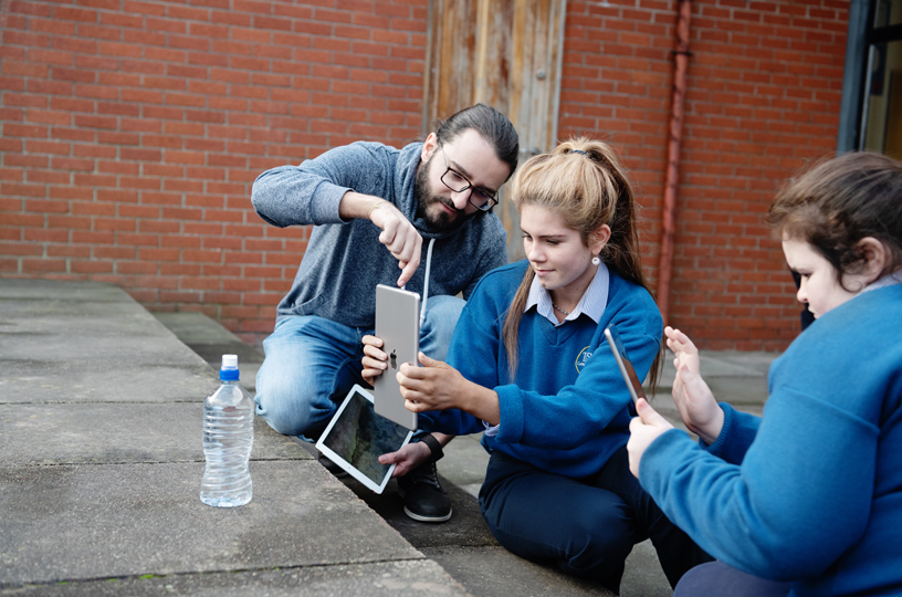 A young woman uses iPad to shoot a photo, with help from an Apple volunteer.