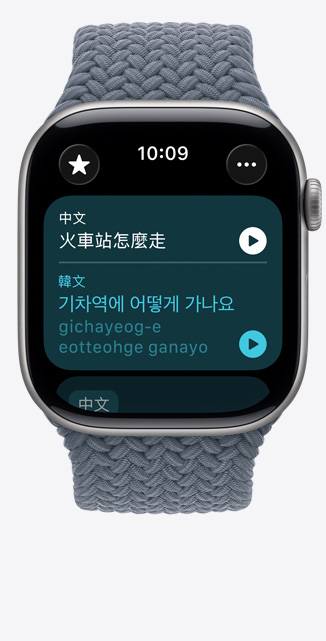 Apple Watch Series 11，展示太空灰色鋁金屬錶殼，搭配錨藍色編織單圈錶環(huán)，螢幕上的「翻譯」app 顯示要怎麼去火車站的韓文翻譯和發(fā)音