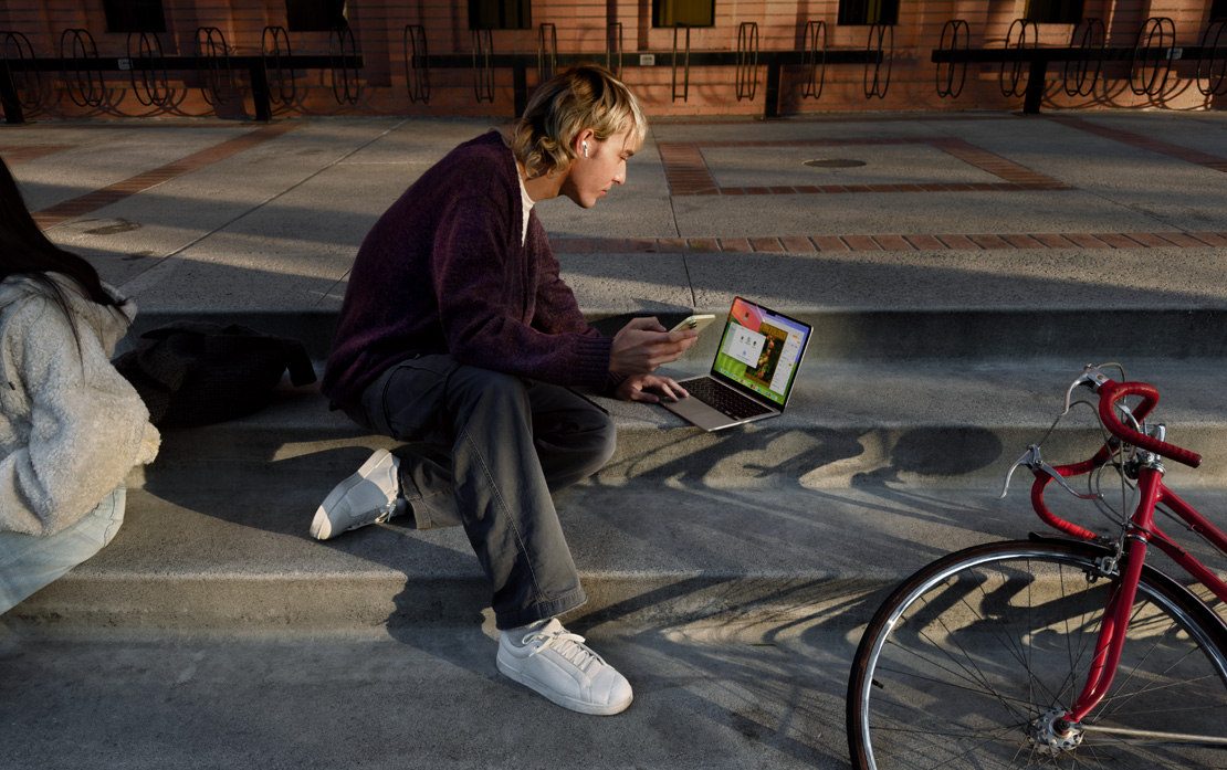自転車のそばで階段に座ってiPhoneとMacBookを使っている學(xué)生