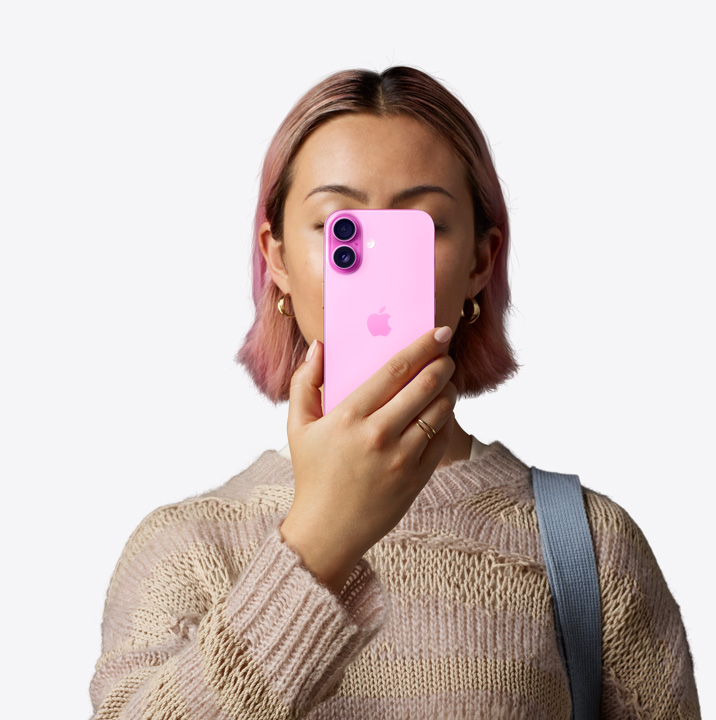 一個(gè)人將粉紅色外觀的 iPhone 16 拿到自己面前，展示機(jī)身背面，雙相機(jī)系統(tǒng)位於左上角。