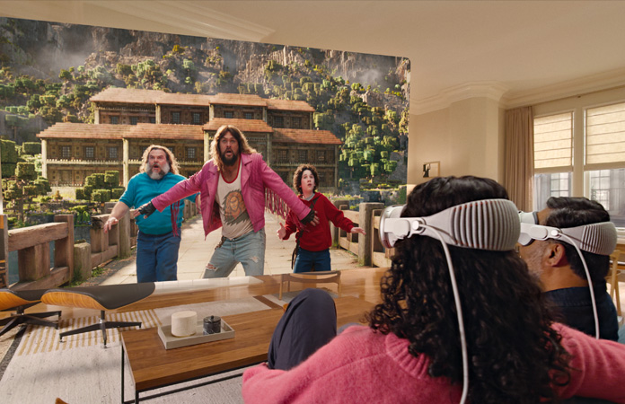 Zwei Personen, die beide jeweils eine Apple Vision Pro tragen, sitzen nebeneinander auf der Couch und schauen: Ein Minecraft Film, gezeigt auf einem Bildschirm, der sich durch den gesamten Raum erstreckt