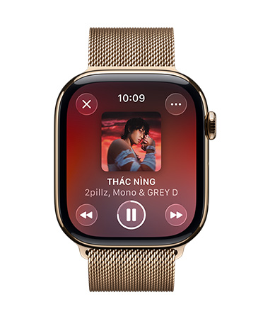 Apple Watch màu Titan Gold v?i day qu?n Milan, m?t ??ng h? hi?n th? Apple Music ?ang phát, nút ?i?u khi?n d?ng Liquid Glass trong m?